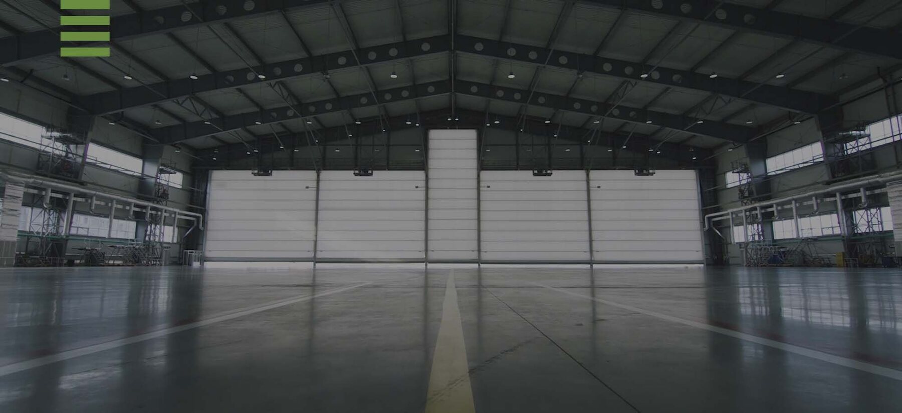 Inside a finished Prairie Barns building: clear span across the full width, four large overhead doors in a row on the end wall, sealed floor.